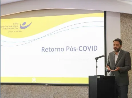 Palestrante homem fala. Tela de projeção mostra capa da palestra Retorno Pós-COVID com logotipo crpg