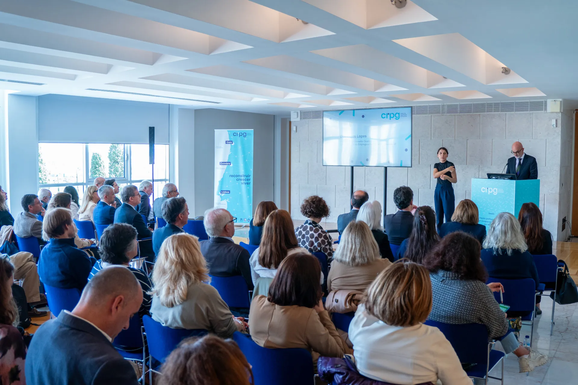 Visão geral da plateia a assistir ao discurso do Presidente do Conselho Diretivo do IEFP – Domingo Lopes, acompanhado com a intérprete de língua gestual.