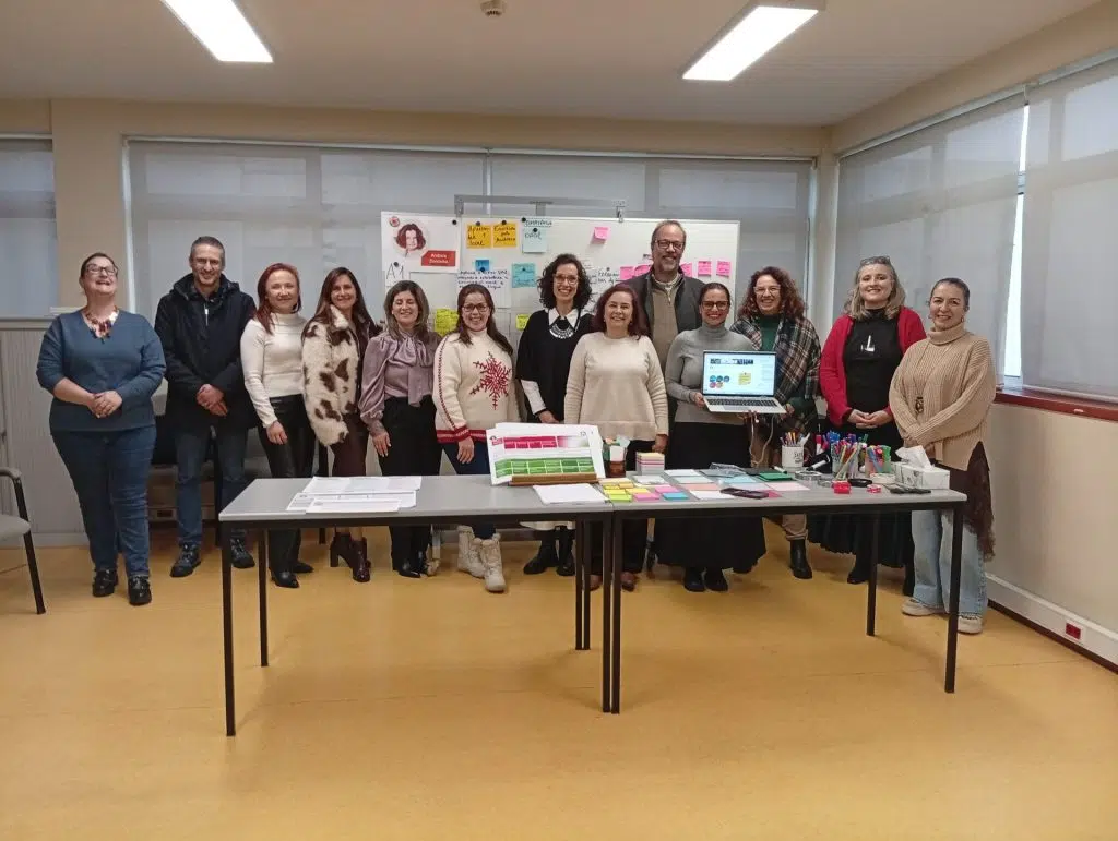 fotografia de grupo de pessoas, em pé, lado a lado, com materiais da formação numa mesa à frente e a sorrirem para a fotografia