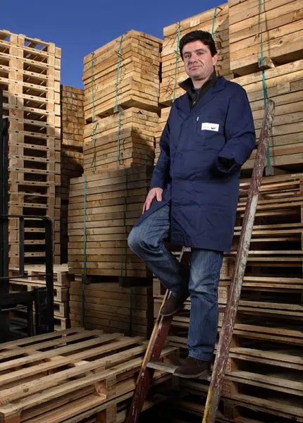 homem amputado em cima de escadote, em frente a paletes empilhadas