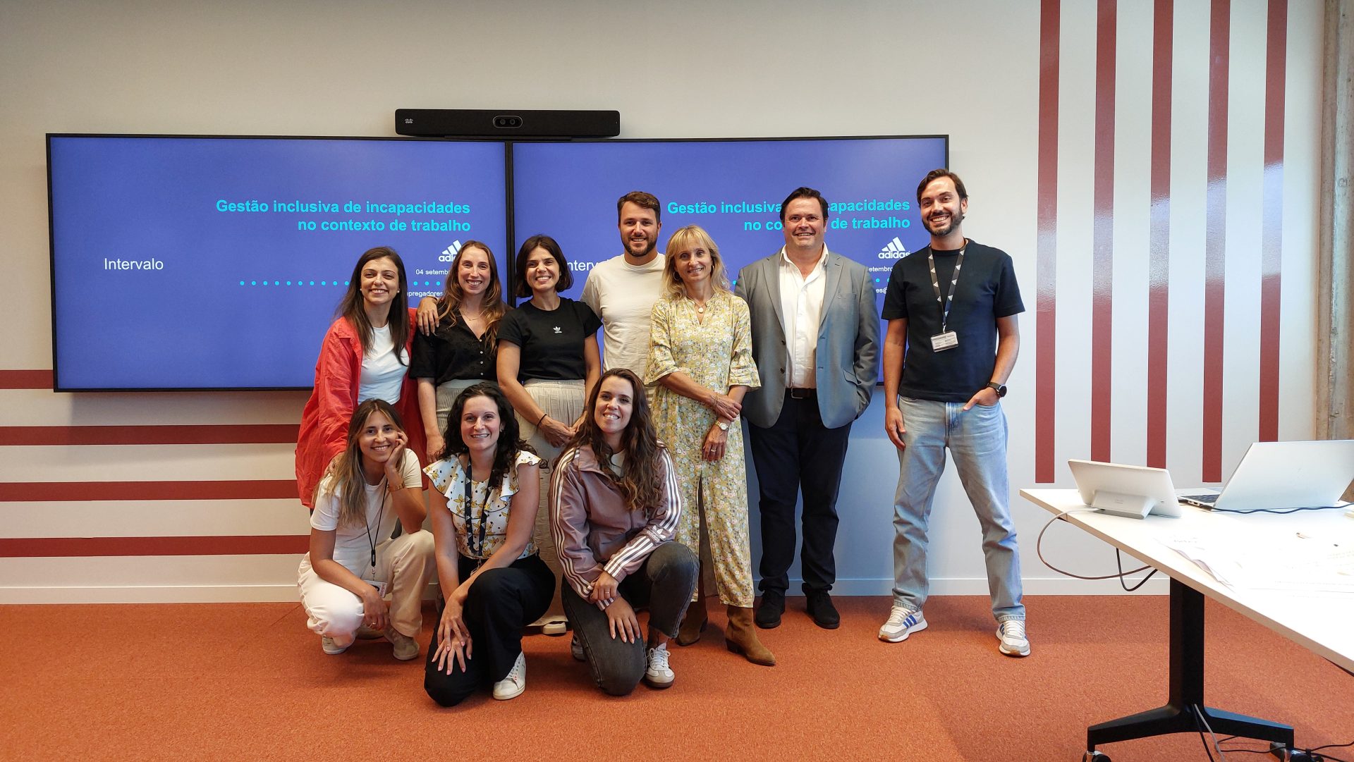 Fotografia de grupo de pessoas a sorrirem para a fotografia com a apresentação da formação no ecrã