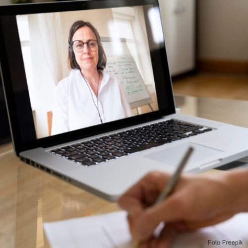Ações de aprofundamento computador portatil em cima da mesa com a imagem de uma pessoa no ecrã à distância