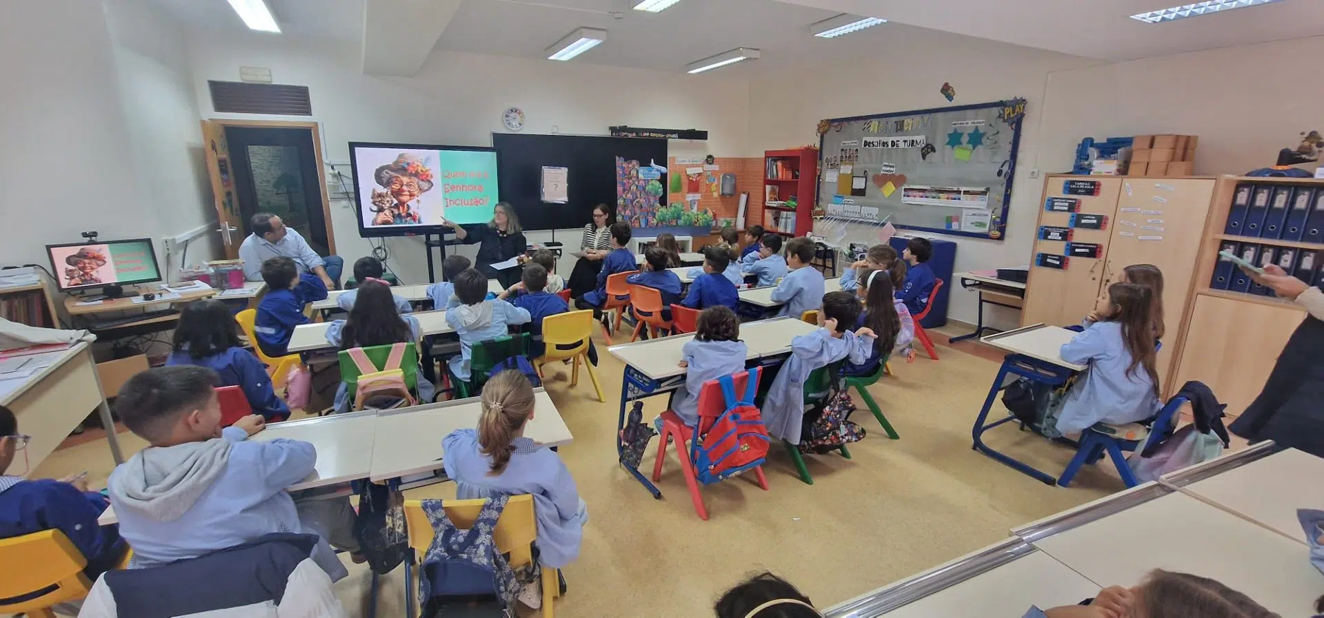 sala de aula, com crianças a olharem para a frente enquanto assistem a apresentação da formadora
