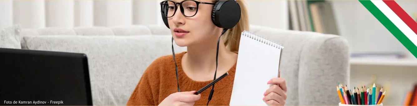 Rapariga à secretária, a olhar para portátil, com lápis e caderno nas mãos.