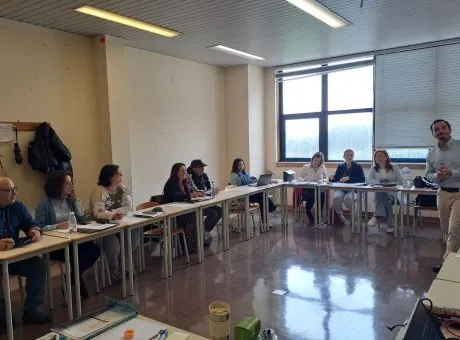 Fotografia numa sala de formação distribuida por mesas lado a lado em forma de U, com pessoas a assistir