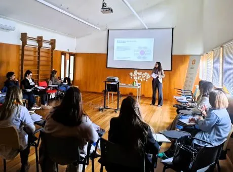 Fotografia de pessoas sentadas a assistir a apresentação de orador com a apresentação a ser projetada na tela