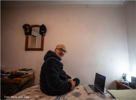 fotografia de pessoa sentada na beira da cama, a olhar para trás com computador portátil em cima da cama