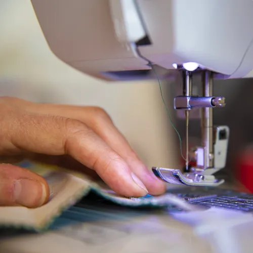 pessoa a colocar um tecido na máquina de costura