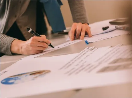 Fotografia onde se visualizam as mãos de uma pessoa a escrever numas folhas
