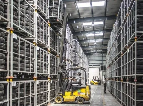 Homens manobram empilhadores em armazém de pneus