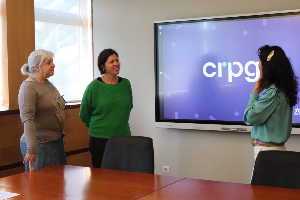 fotografia 3 pessoas em pé a conversar com um ecrã no fundo com o logotipo do CRPG