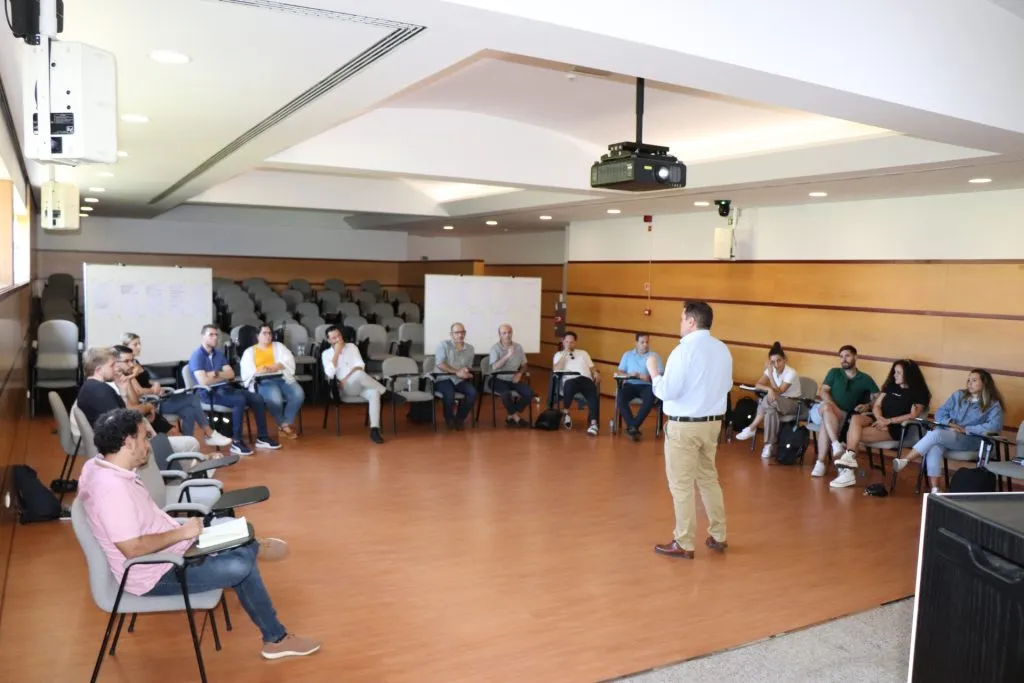fotografia durante a ação. Pessoas sentadas lado a lado em formato de semicirculo a assistir a apresentação