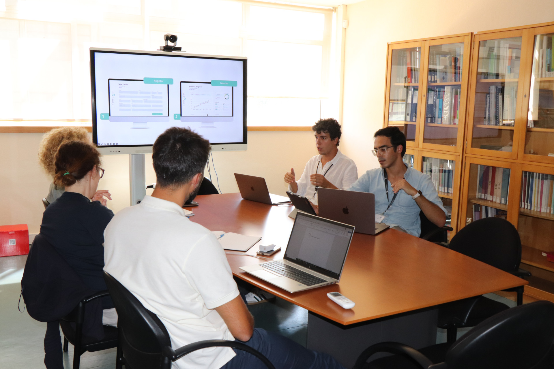 fotografia de 4 pessoas sentadas à mesa a conversar e apresentação no quadro interativo