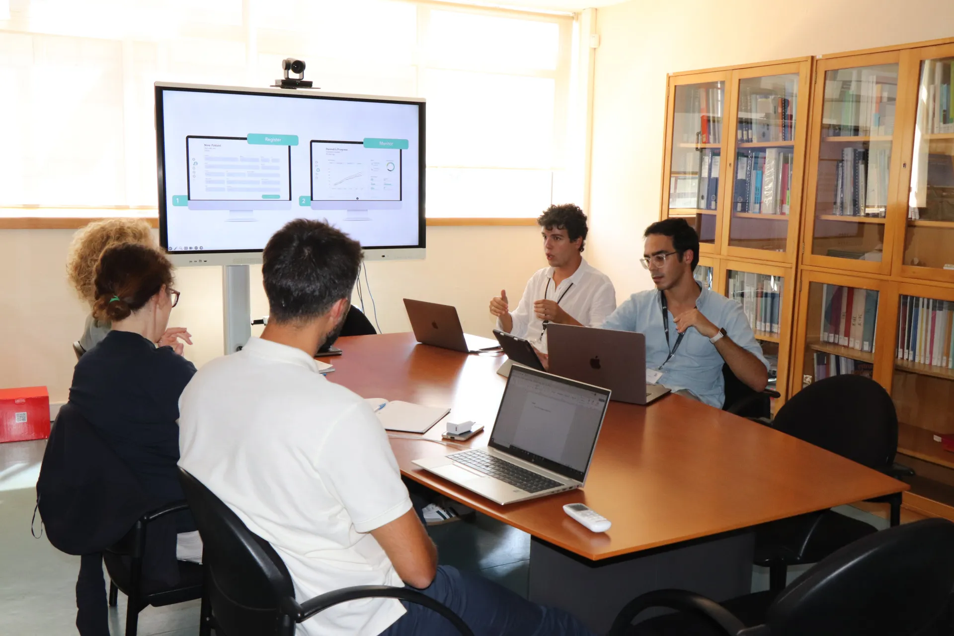 fotografia de 4 pessoas sentadas à mesa a conversar e apresentação no quadro interativo