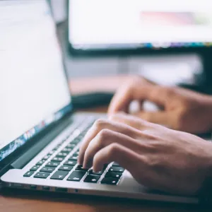 Imagem de duas mãos a escrever no teclado de um portátil.