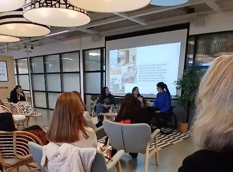 Fotografia de pessoas sentadas a assistir a conversa entre três pessoas com projeção nas costas