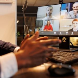 fotografia de pessoa à secretaria durante uma sessão online, com o teclado e monitor à sua frente
