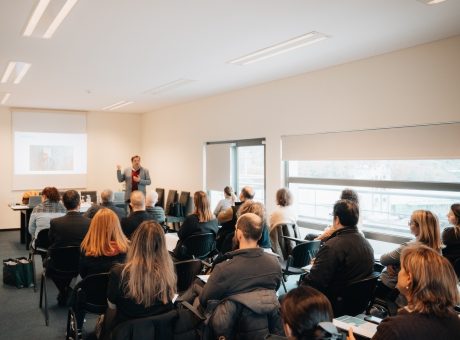 fotografia de pessoas sentadas a assistir a apresentação projetada na parede e orador em pé