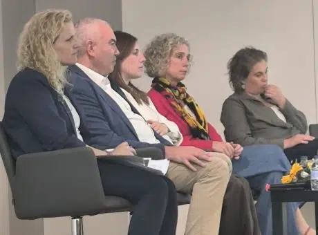 5 pessoas sentadas. lado a lado, enquanto assistem a apresentação