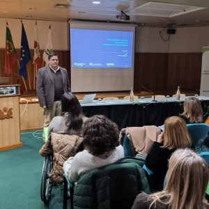 grupo de pessoas sentadas a assistir a apresentação de orador em pé à frente