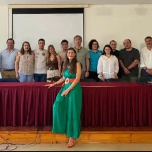 fotografia de grupo de pessoas, lado a lado, em pé, a sorrirem para a fotografia, atrás de uma mesa comprida com uma tolha bordeaux