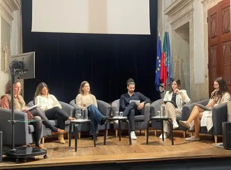 Fotografia de 6 pessoas sentadas em poltronas colocadas num palco enquanto conversam