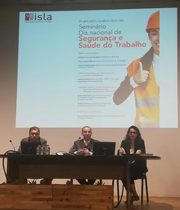 Oradores em mesa, em cima do palco durante Seminário do Dia nacional da Segurança e Saúde do Trabalho