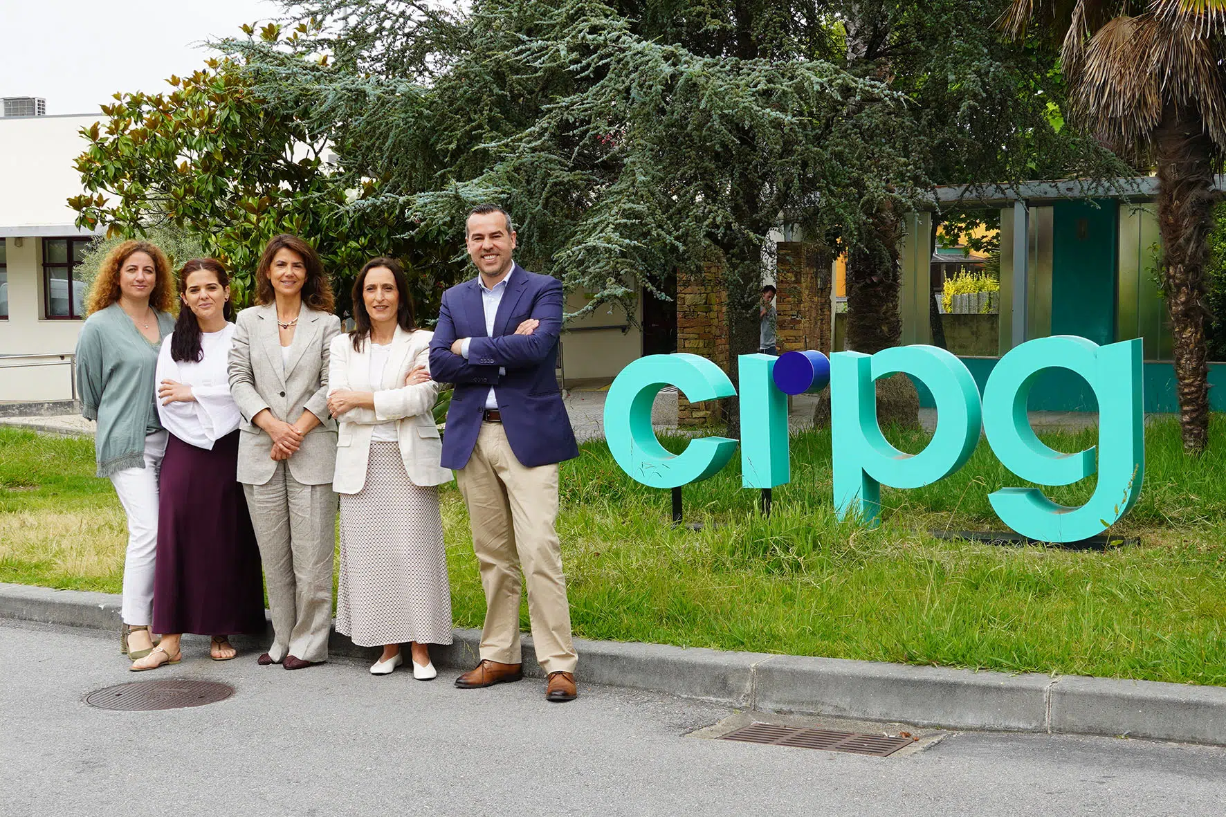 Visita2026-06-18-F3 5 pessoas, lado a lado, em pé, à frente de um jardim com as letras do CRPG, a sorrirem para a fotografia